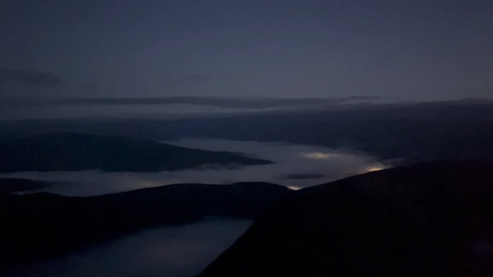 Pre-dawn view from the flank of Ben Nevis, a sea of fog settled into the valley with lights glowing underneath